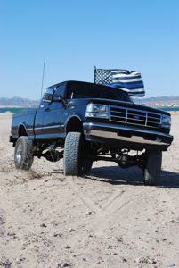 Noah's lifted black 1997 Ford F250 with Thin Blue Line flag parked in a desert landscape