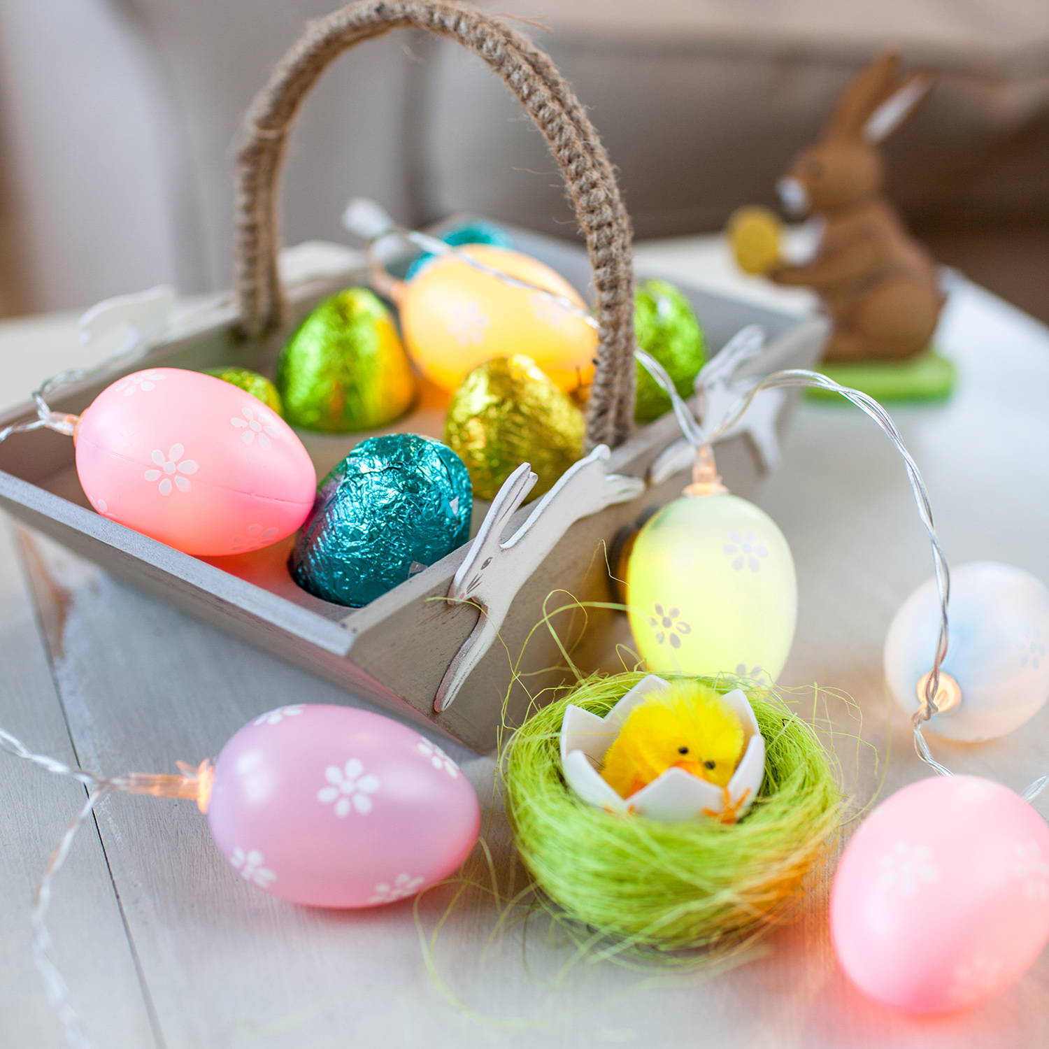 Pastel egg Easter fairy lights styled as part of Easter basket display with mini chocolate eggs and mini chick in nest 