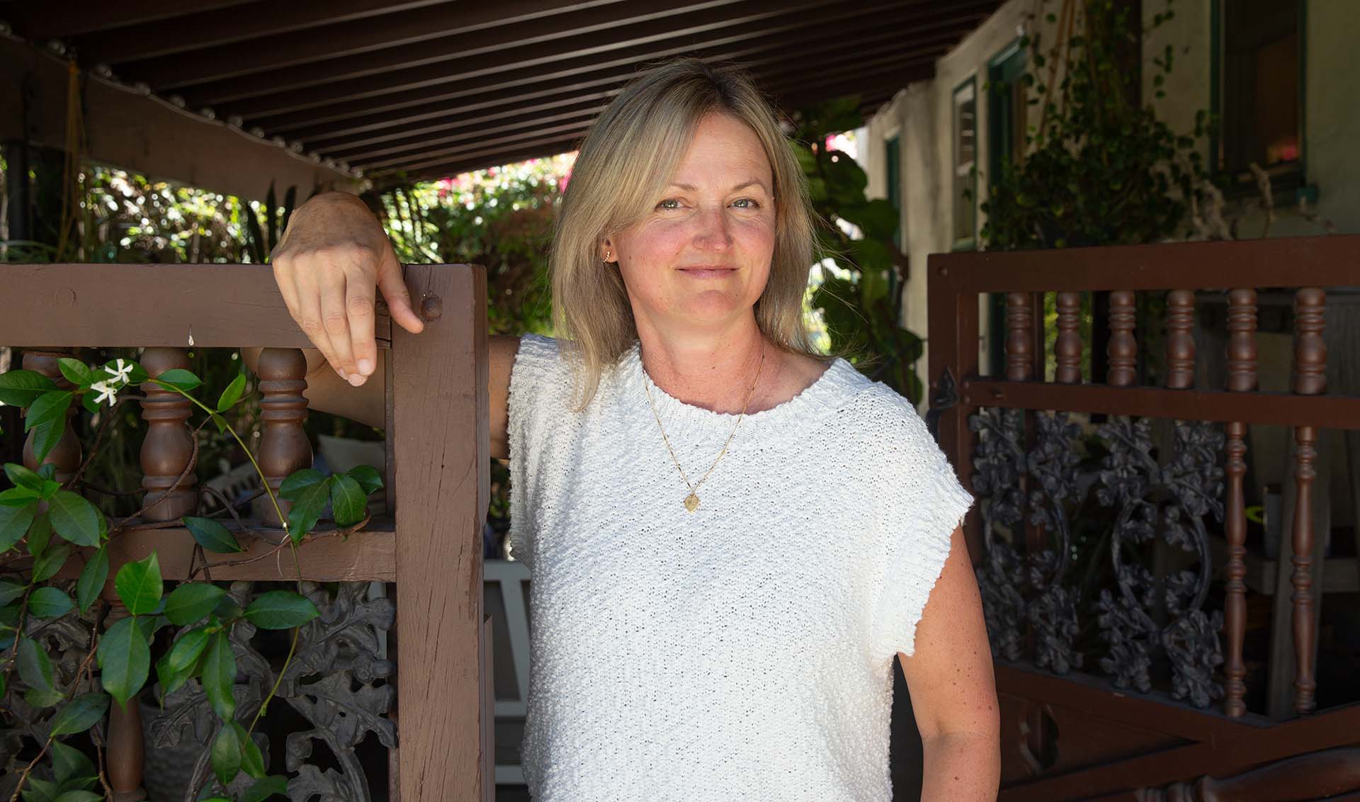 A portrait of Jen Dunbar, historic preservation architect. She's standing at a carved wood gate with climbing ivy.