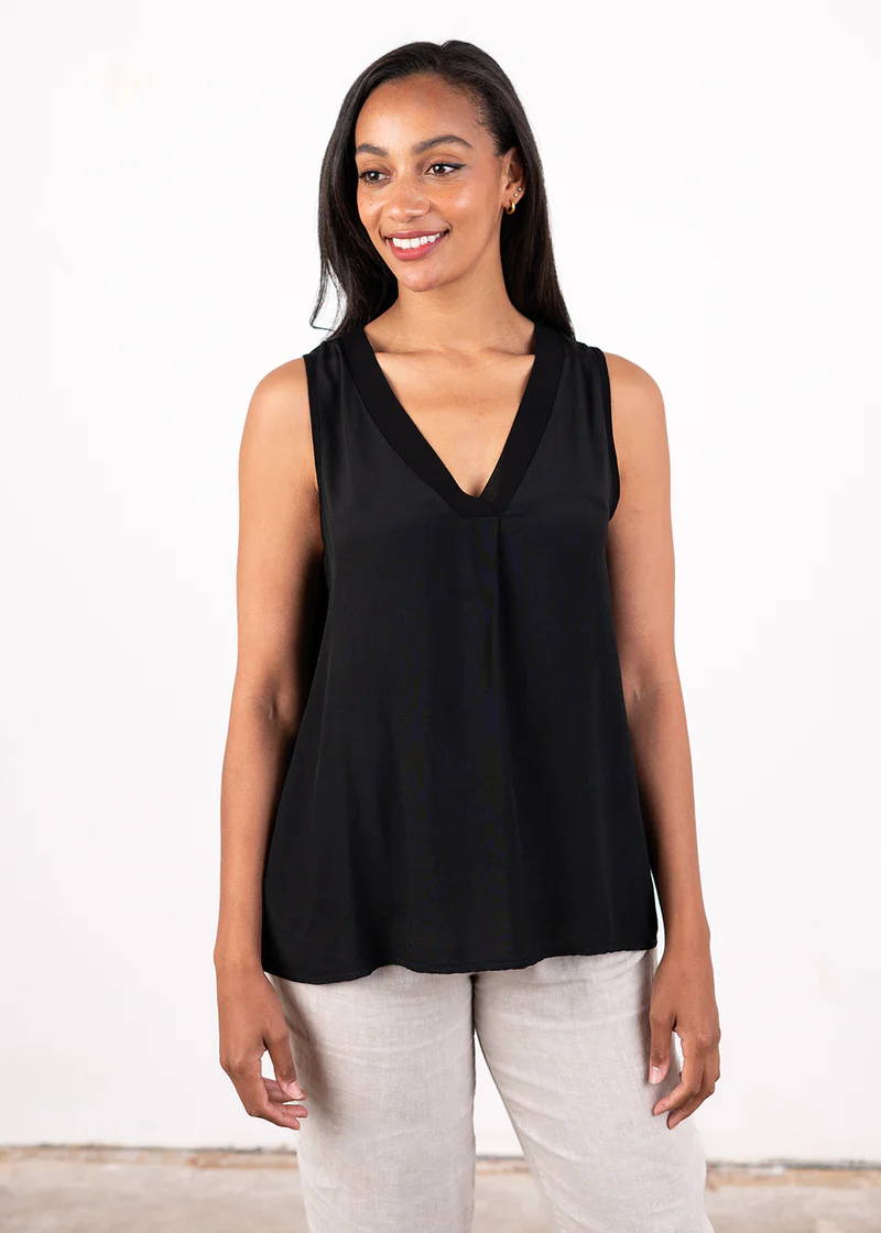 A model wearing a black, sleeveless top with a v neckline over off white trousers