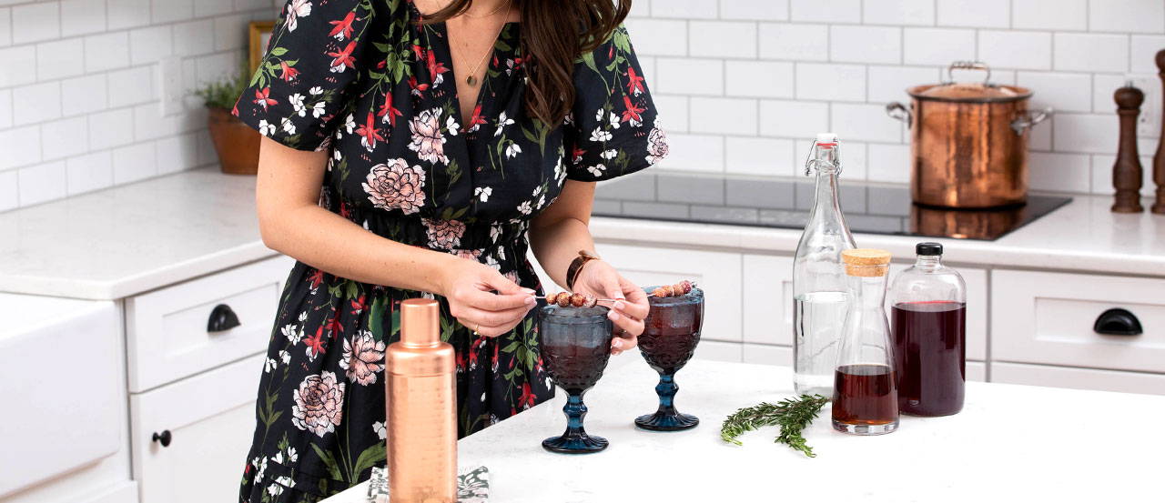 Woman making cocktails with jewel tone vintage glasses