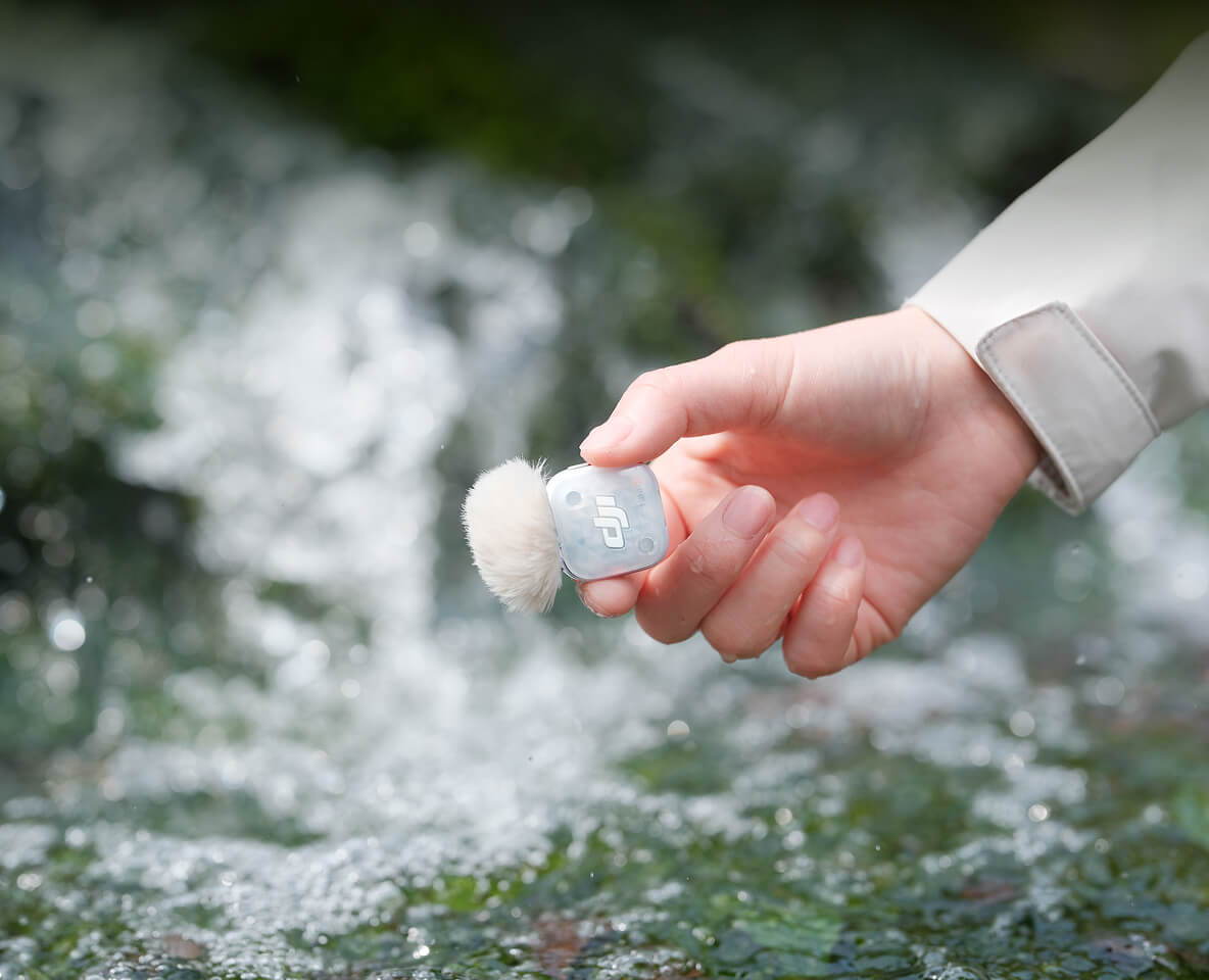 A hand holding a DJI Mic Mini 2S over flowing water.