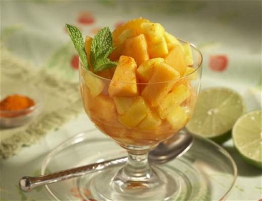 A glass bowl of mango salad garnished with mint leaves and lime slices.