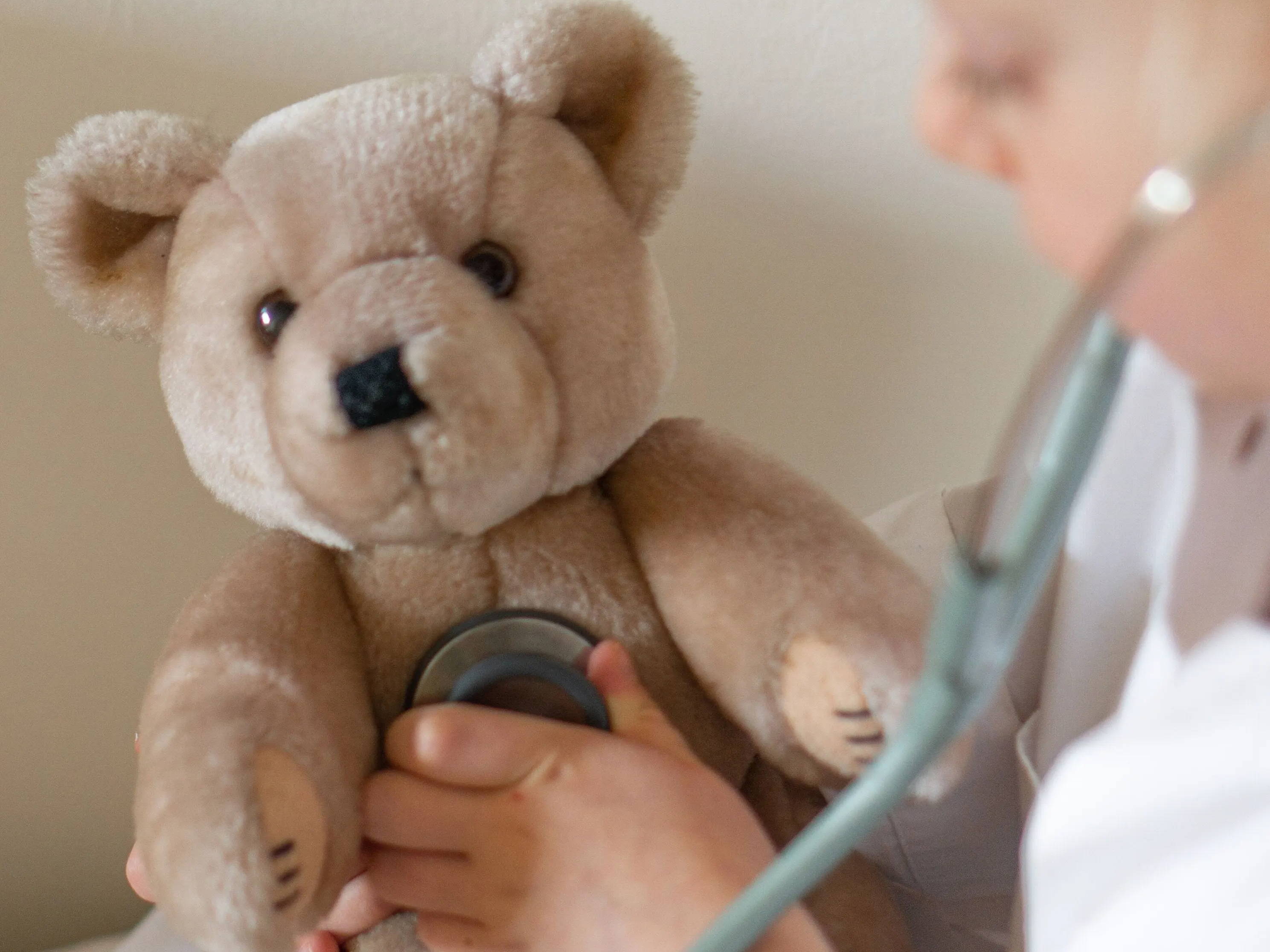 Enfant portant un manteau blanc jouant au médecin - il utilise un stéthoscope pour examiner son ourson en peluche