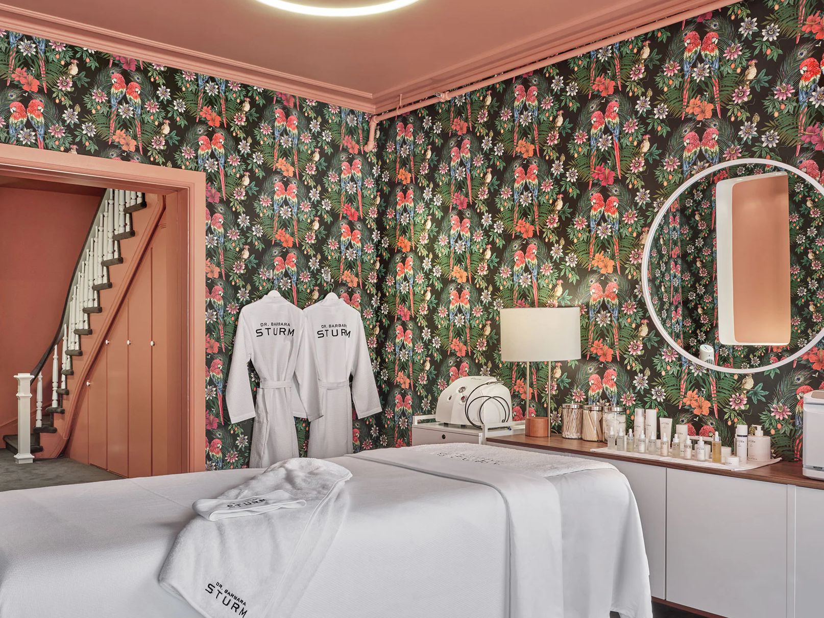 Spa treatment room with floral wallpaper and robes hanging.