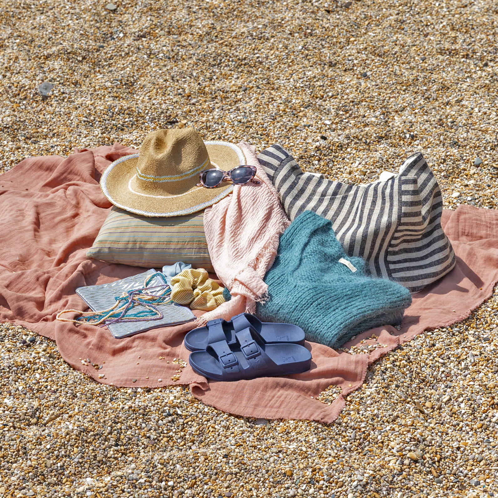 A flat lay of a picnic mat on a beach with a knitted blue jumper and summer accessories