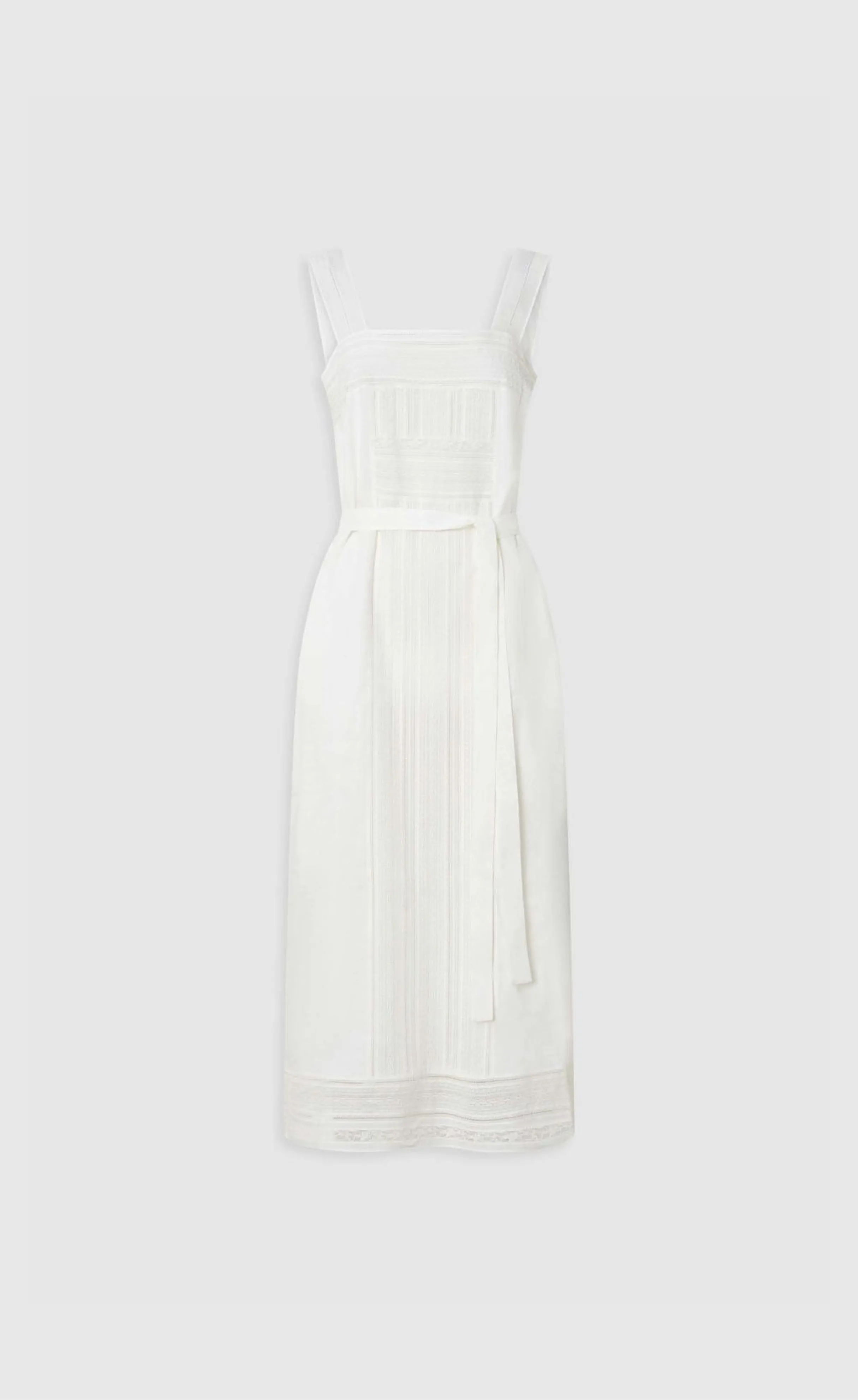White sleeveless dress with a tied waist and intricate detailing.