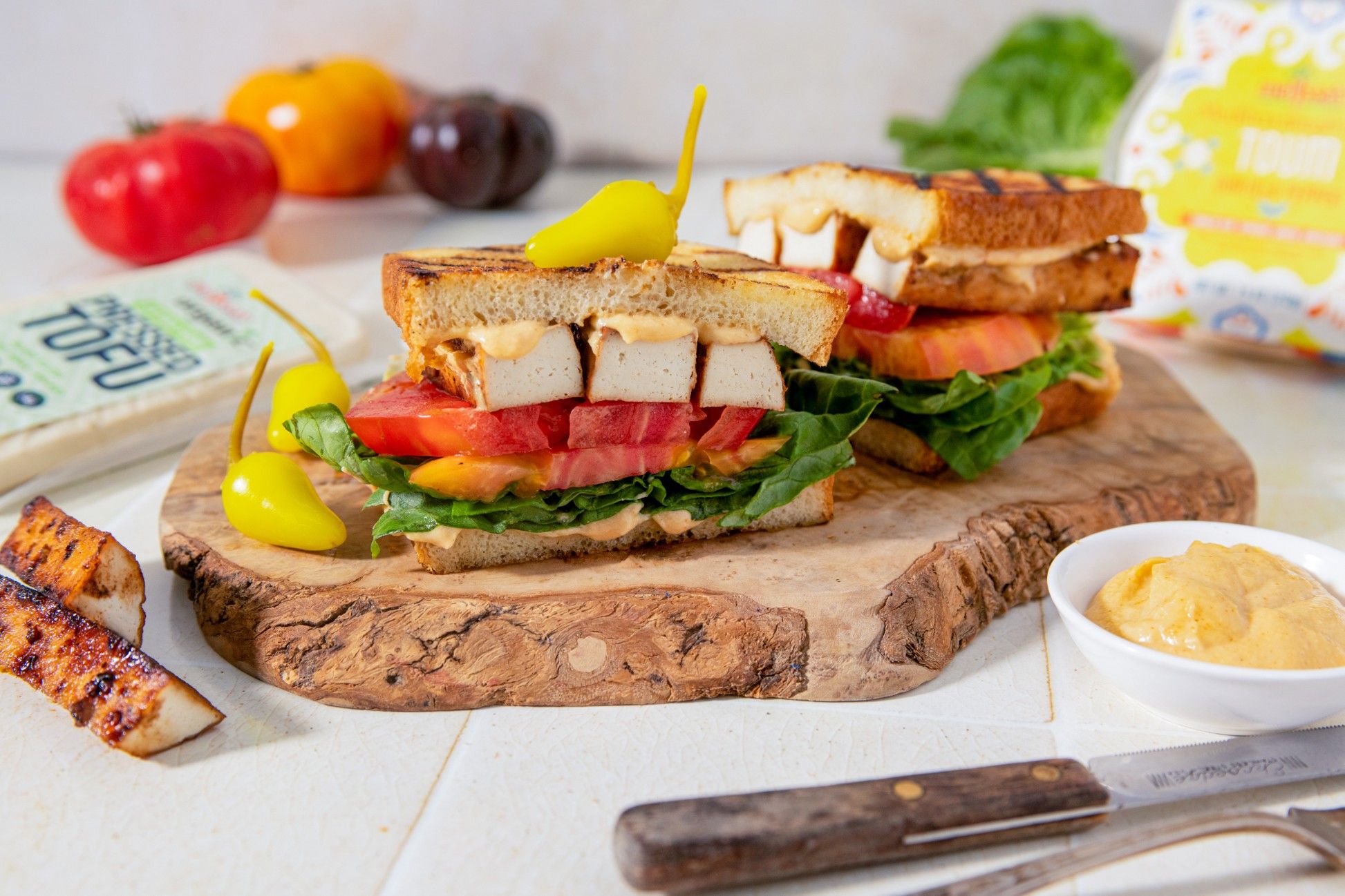 A sandwich with chicken, lettuce, tomato, and a side of hummus.