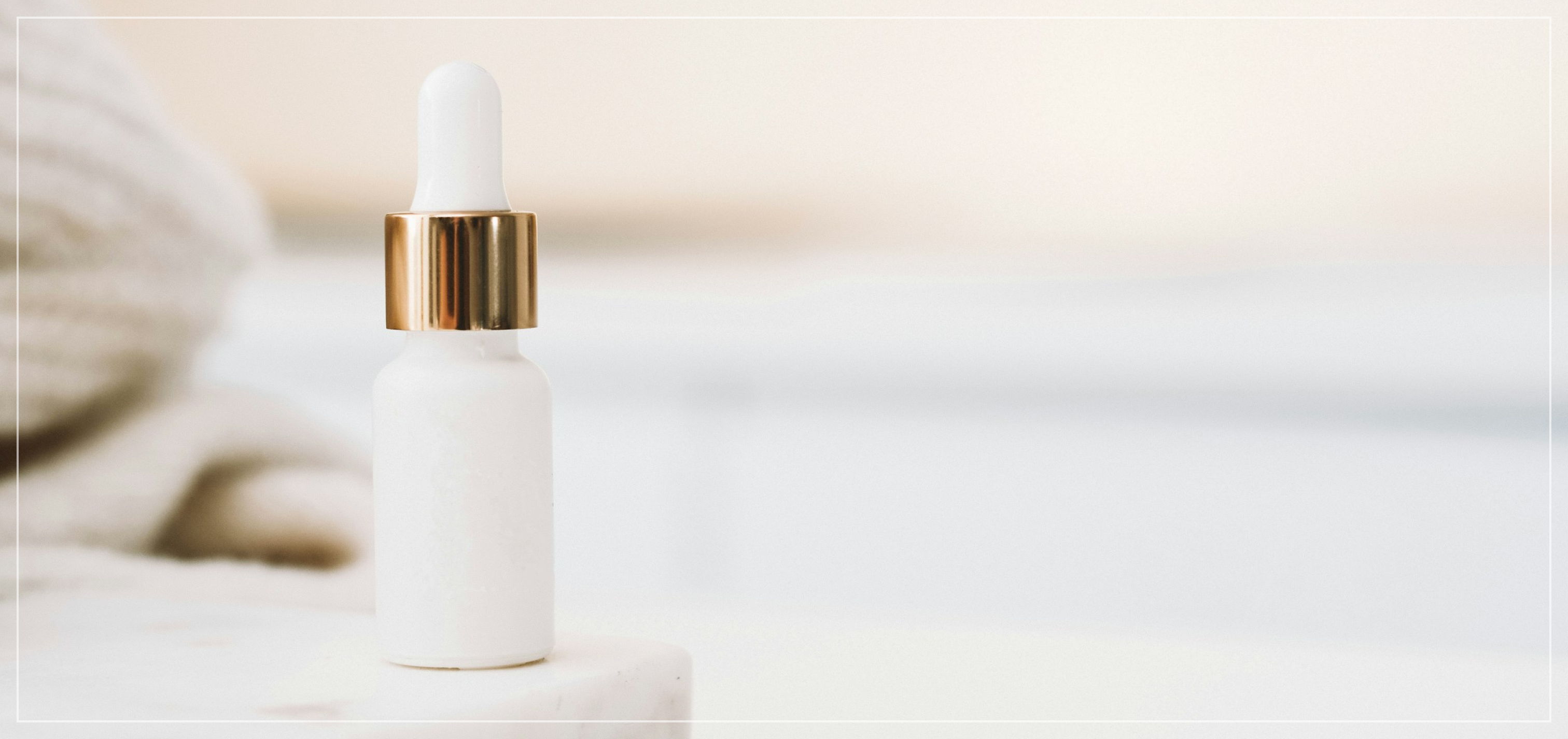 A white and gold makeup bottle sat on a marble surface, with an out of focus towel in the background