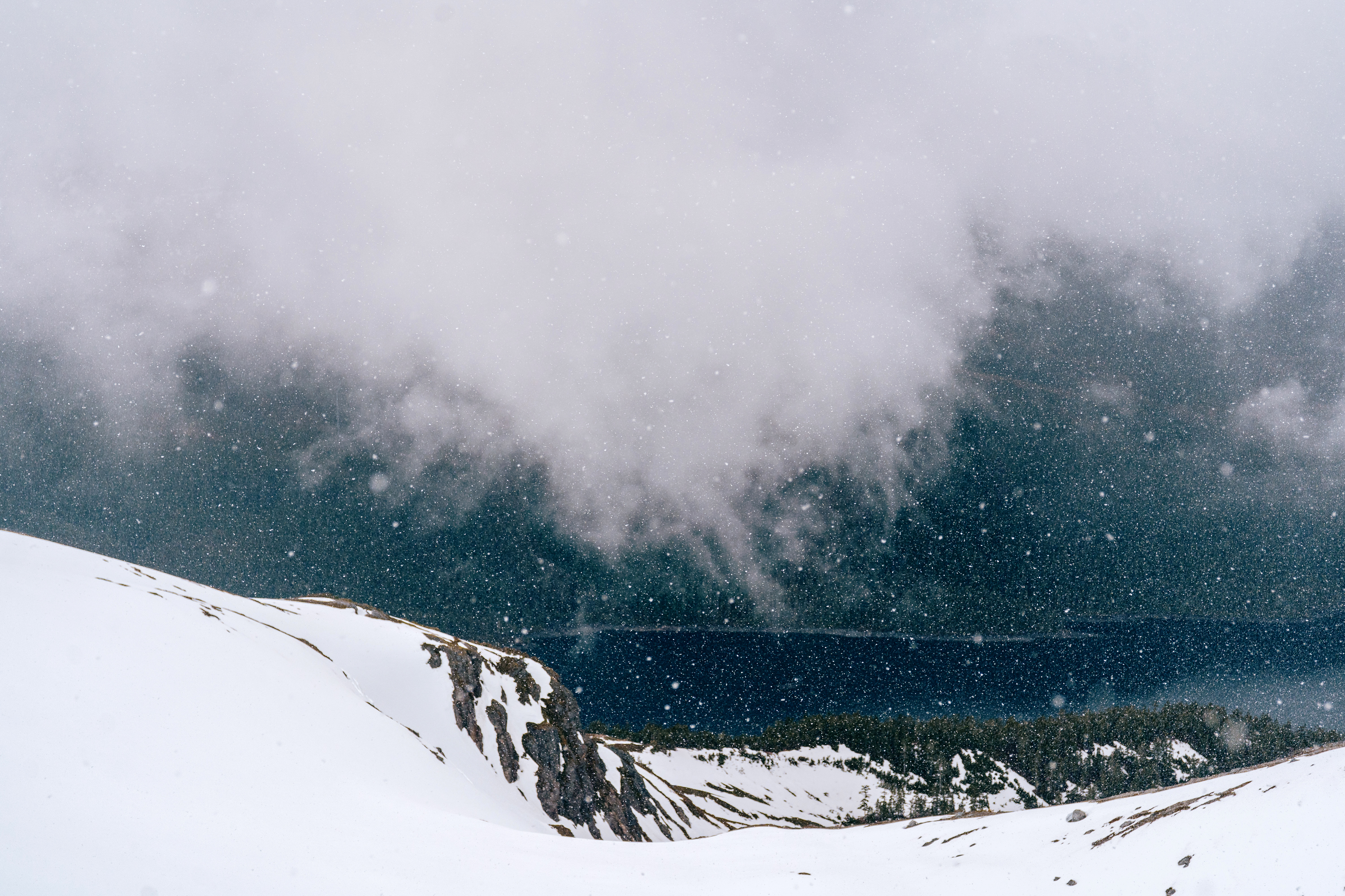 Snowy mountain landscape with clouds and a body of water below.