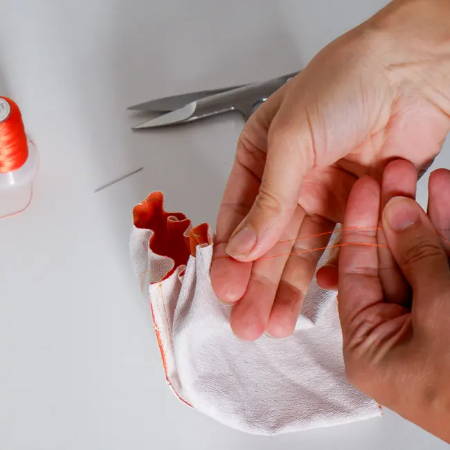 Hands pulling orange thread to gather the fabric of a fabric tube