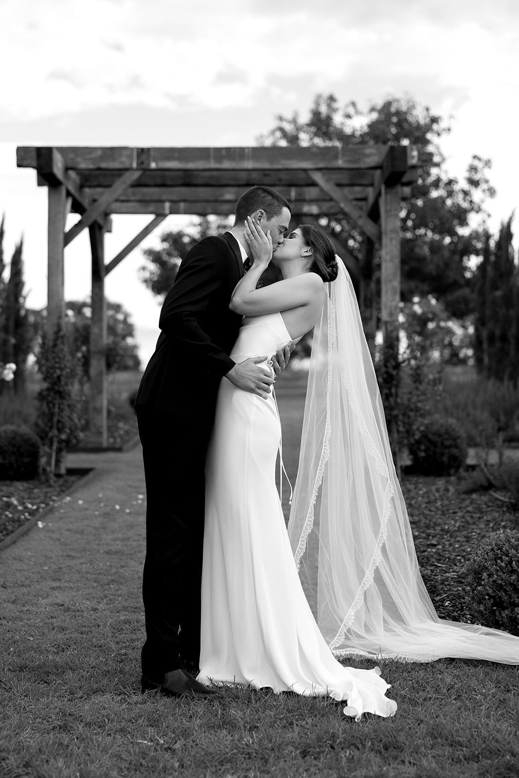 A bride and groom sharing a kiss under an arbor. Black and white photo.