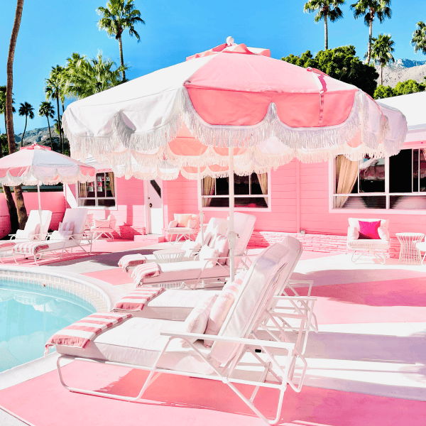 Pink fringed patio umbrella at the Trixie Motel pool, adding playful shade to a colorful Palm Springs outdoor lounge.