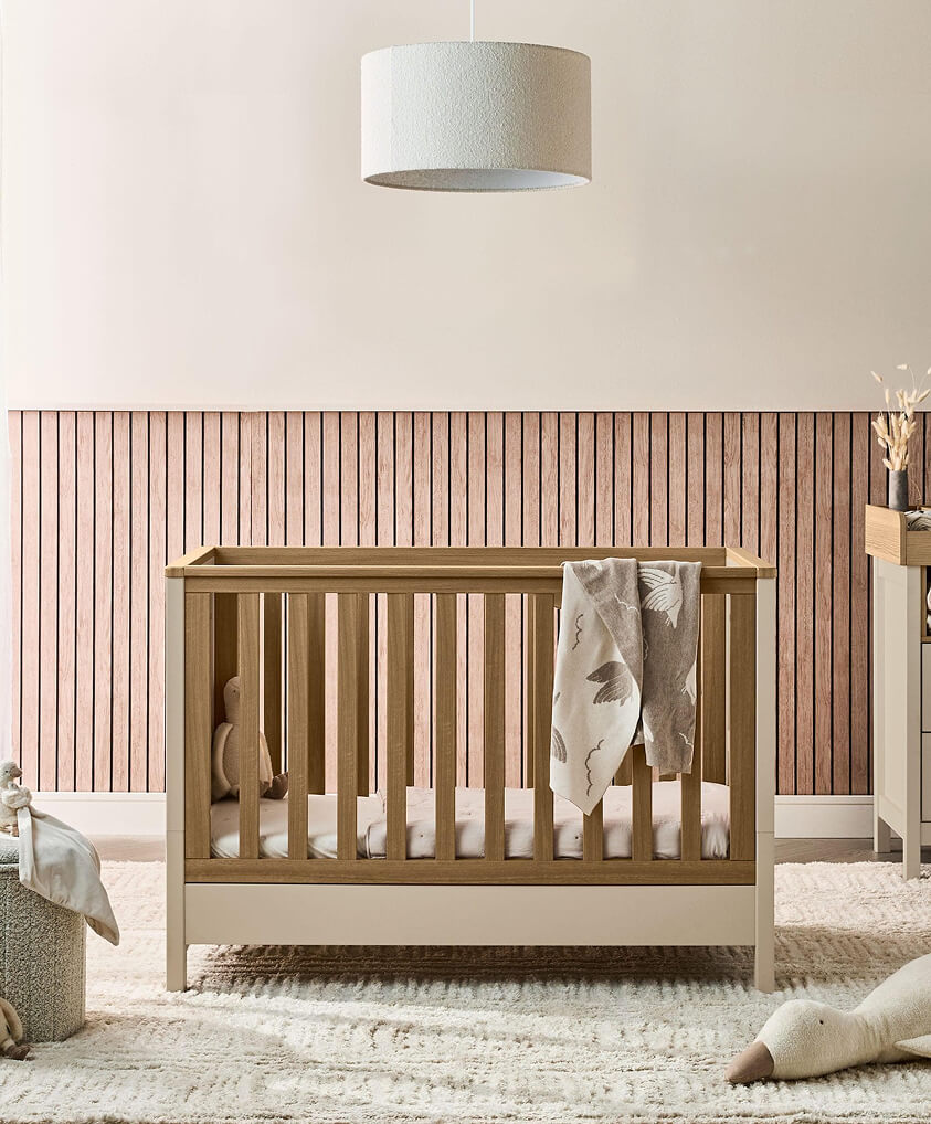 A cozy nursery with a wooden cotbed and soft decor.
