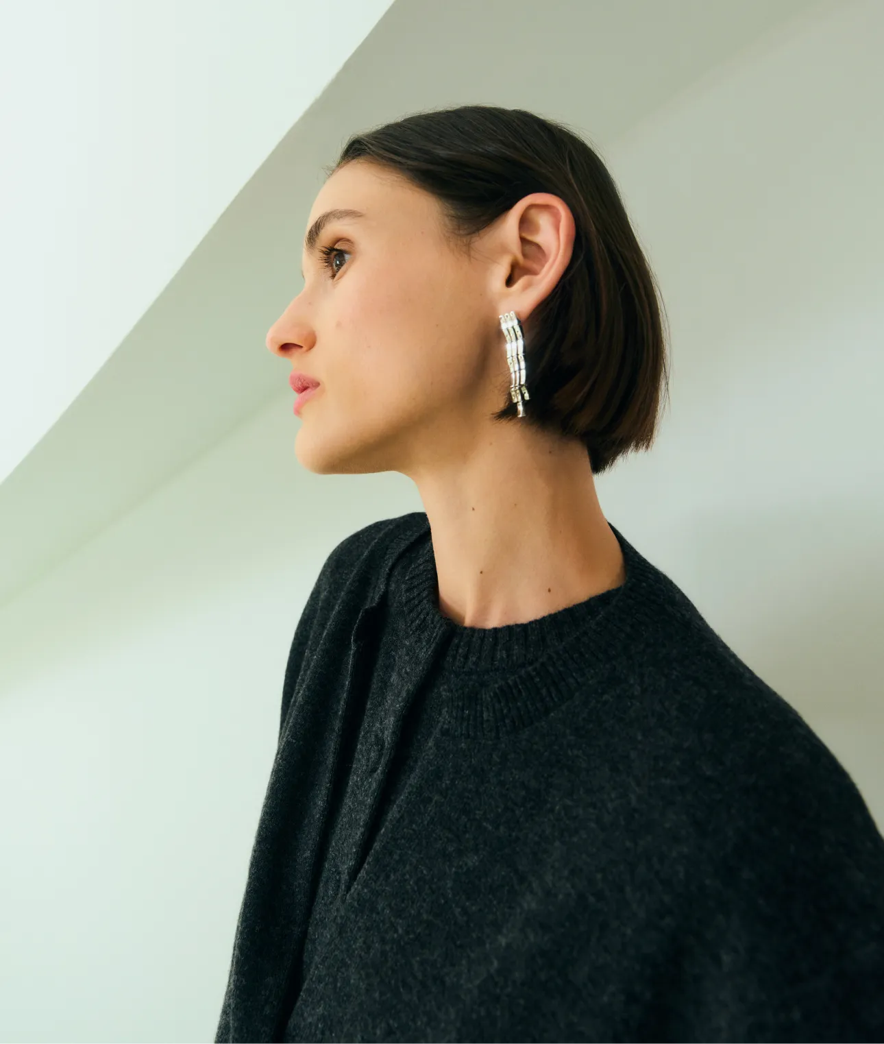 A woman in a dark sweater, wearing silver earrings, looking to the side.
