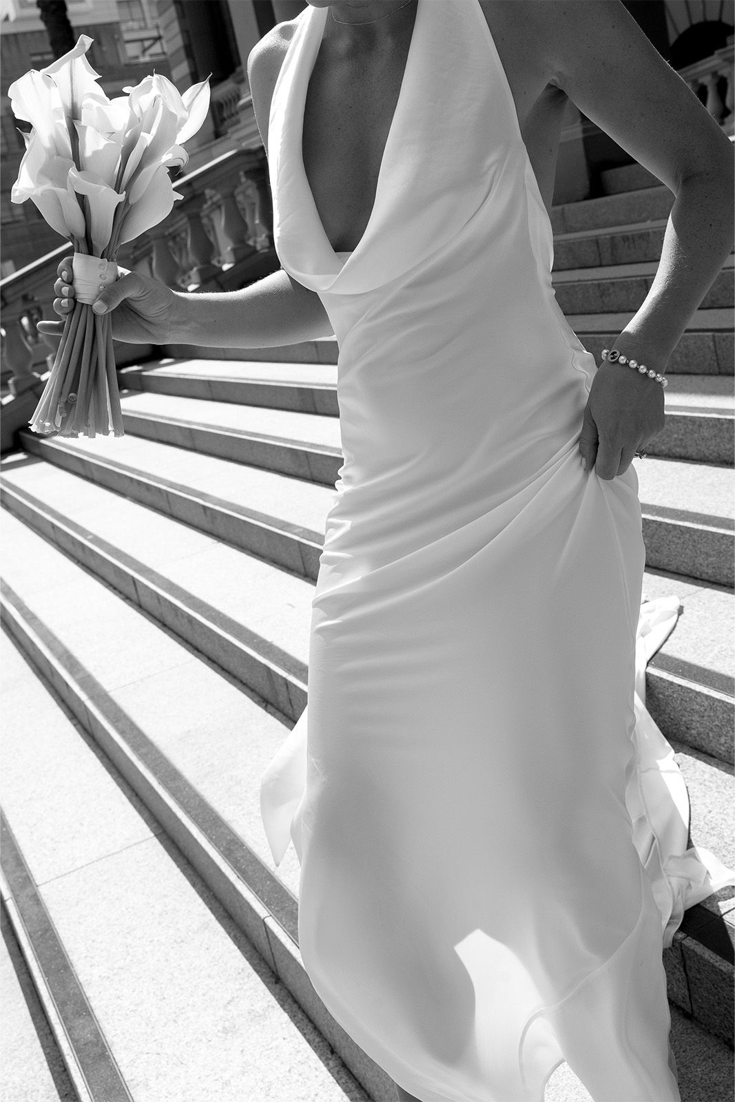 Bride in a white dress holding a bouquet, walking down stairs.