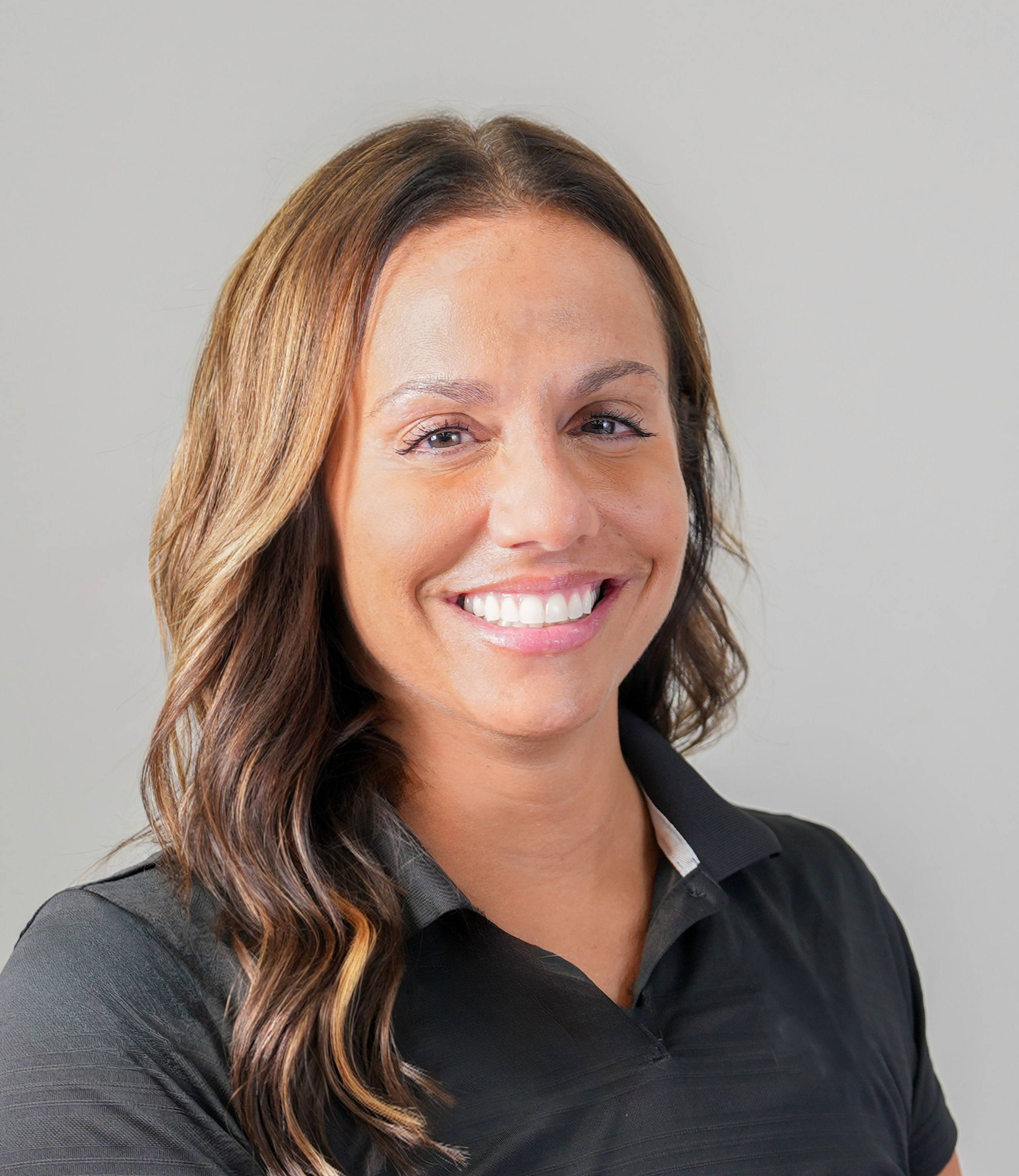 Smiling woman in a black polo shirt against a gray background.