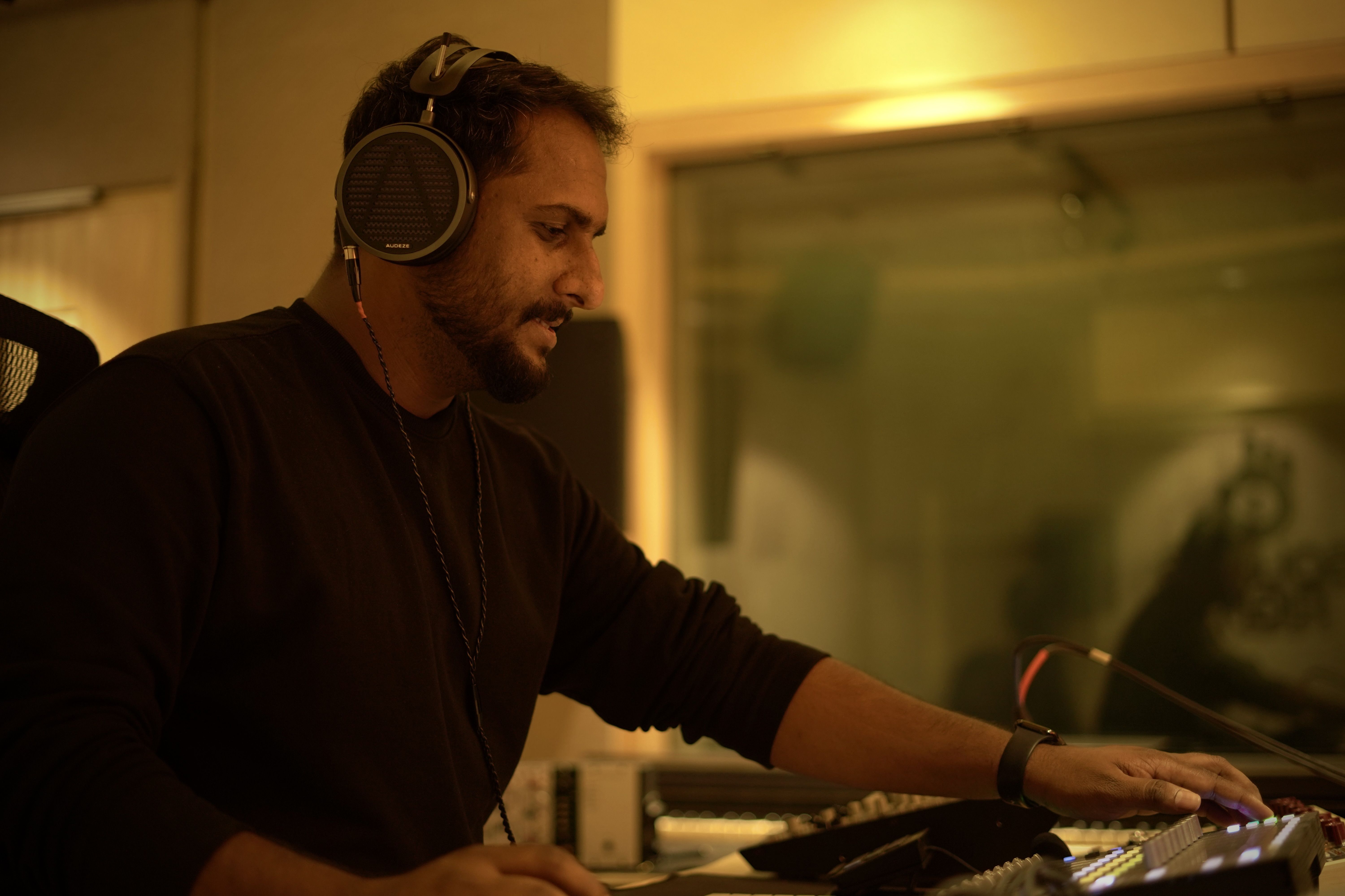 Aswin John wearing Audeze MM-500 headphones working at a sound mixing console in a studio.