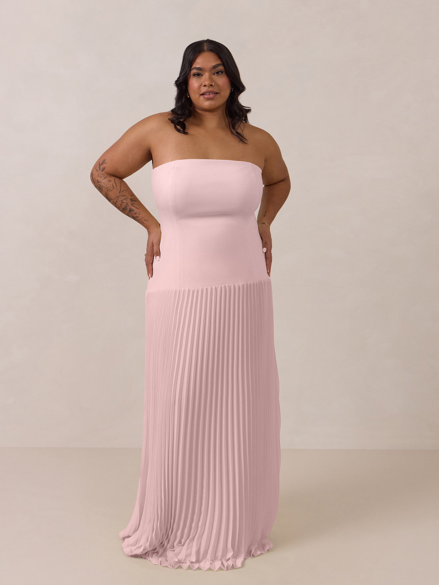 Woman in a strapless pink gown standing against a neutral background.