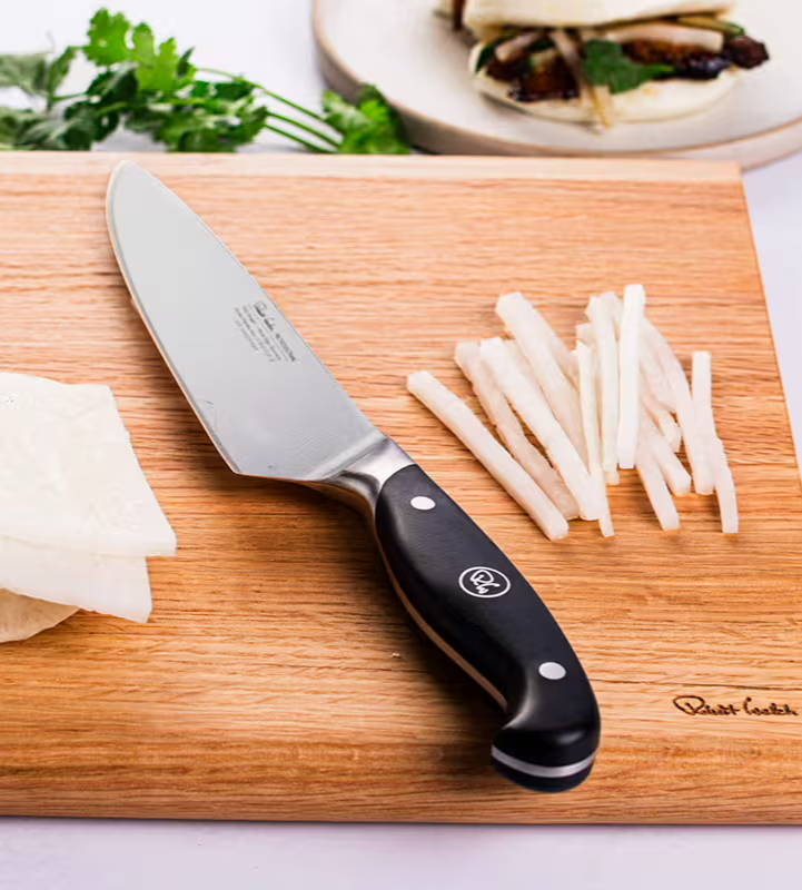A Professional kitchen knife on a wooden cutting board with sliced mushrooms.