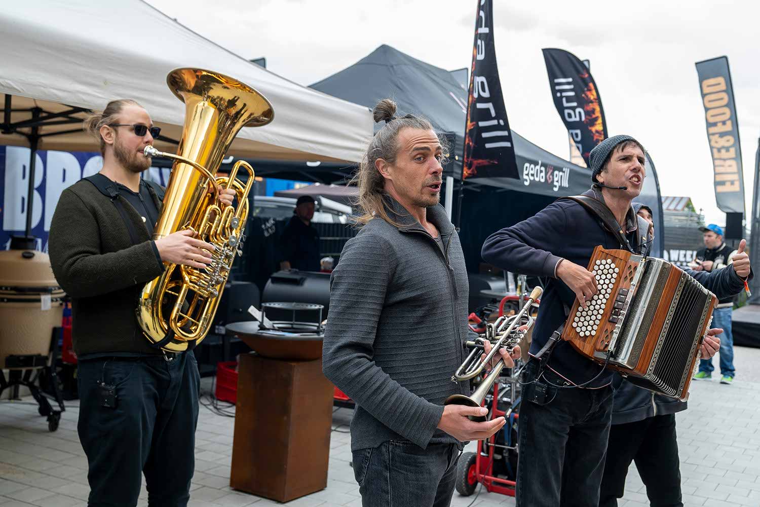 Three musicians playing instruments outdoors at an event.