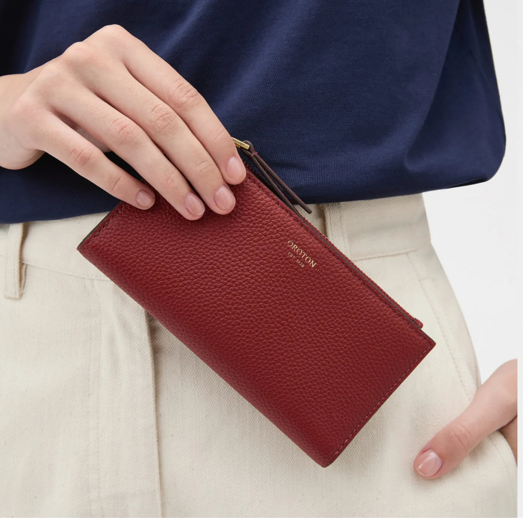 Hand holding a red wallet against a blue shirt and light-colored pants.