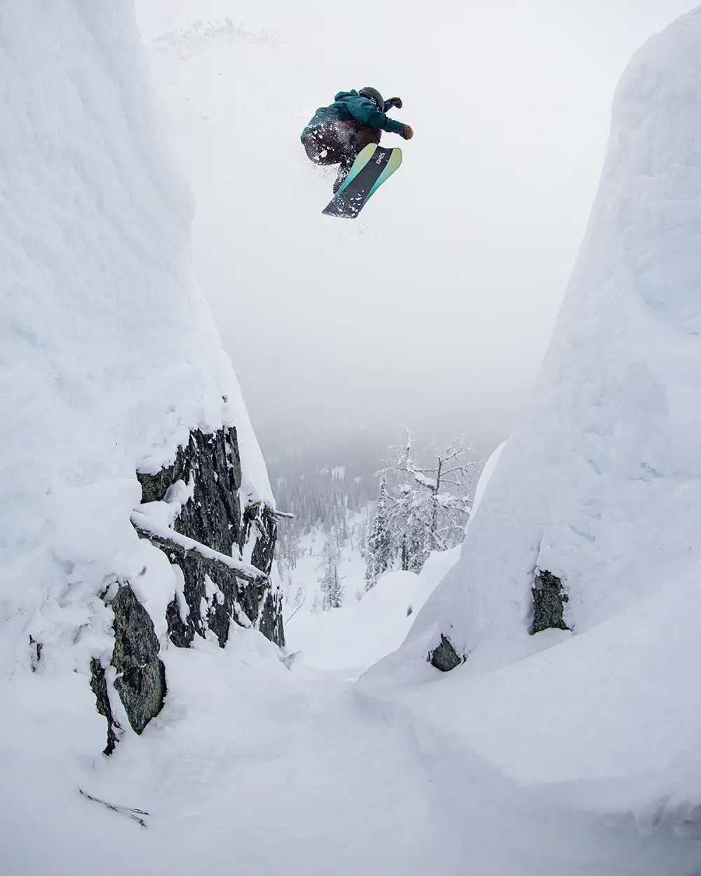 Snowboarder jumping between snow-covered cliffs in a winter landscape.