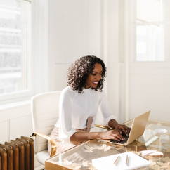 woman sitting in a white chair and shirt, work desk, typing on laptop, paper, pens