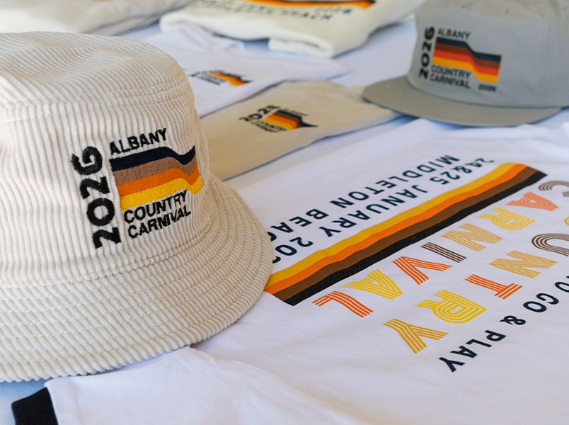 A merch bundle for Albany Country Carnival featuring multicolour striped logo design embroidered on a cream corduroy bucket hat, screen printed on tees, and DTF transfered onto surf cap
