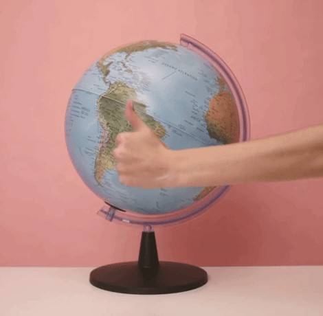 Fotografia do globo terrestre e uma mão com o polegar levantado na frente do globo