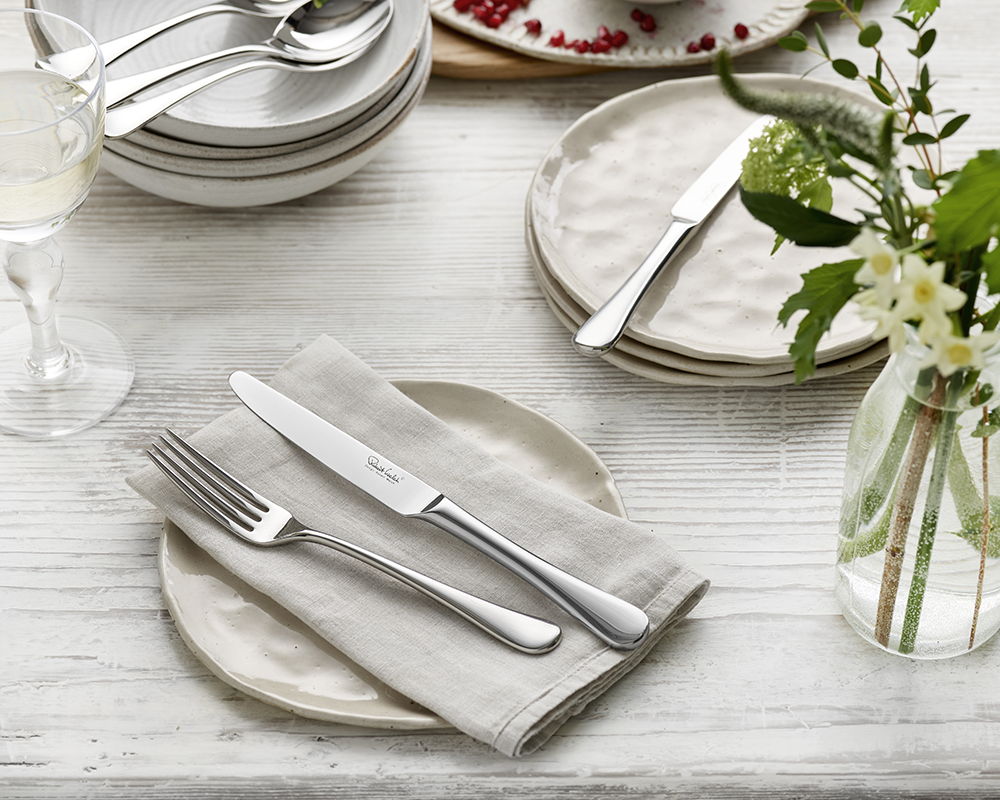 Table setting with plates, Radford Bright cutlery, and a vase of flowers.