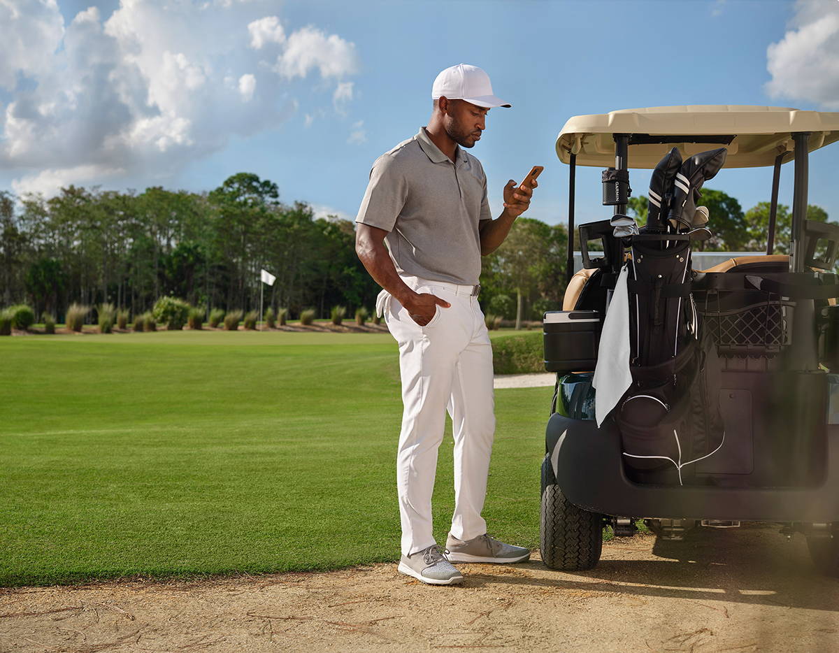 A golfer standing next to his cart looking at his phone with  the Garmin Approach Z82 golf rangefinder