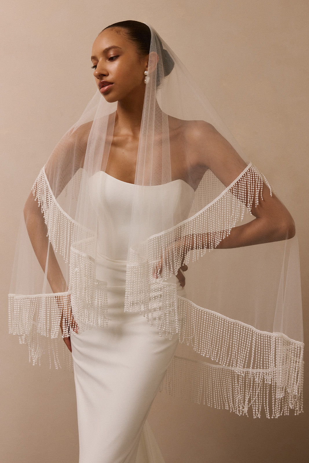 Bride in elegant white dress with fringed veil, posing gracefully.