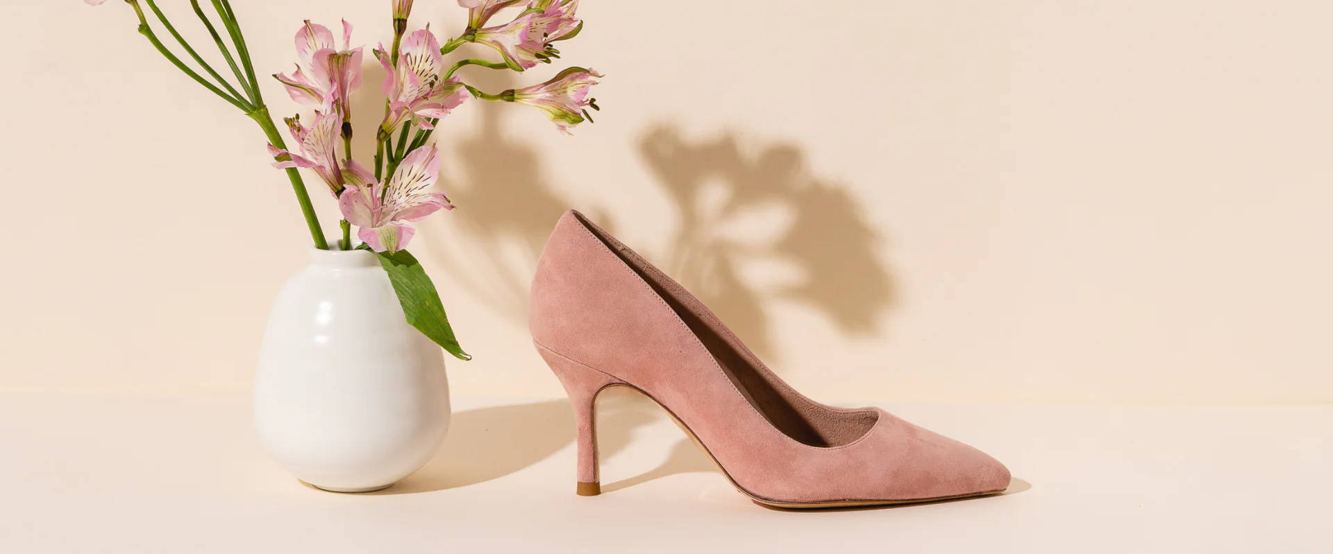 A pink high heel shoe next to a vase of flowers.