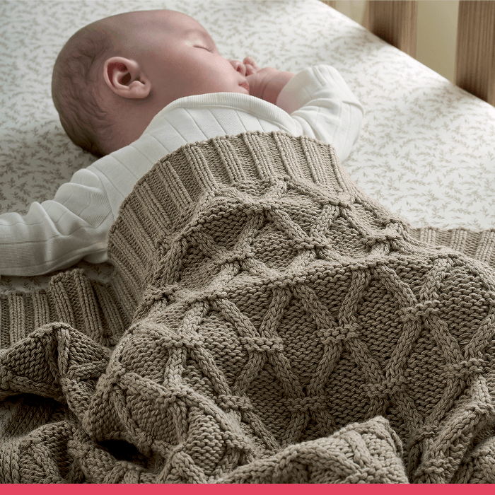 Baby peacefully sleeping under a knitted blanket in a crib.