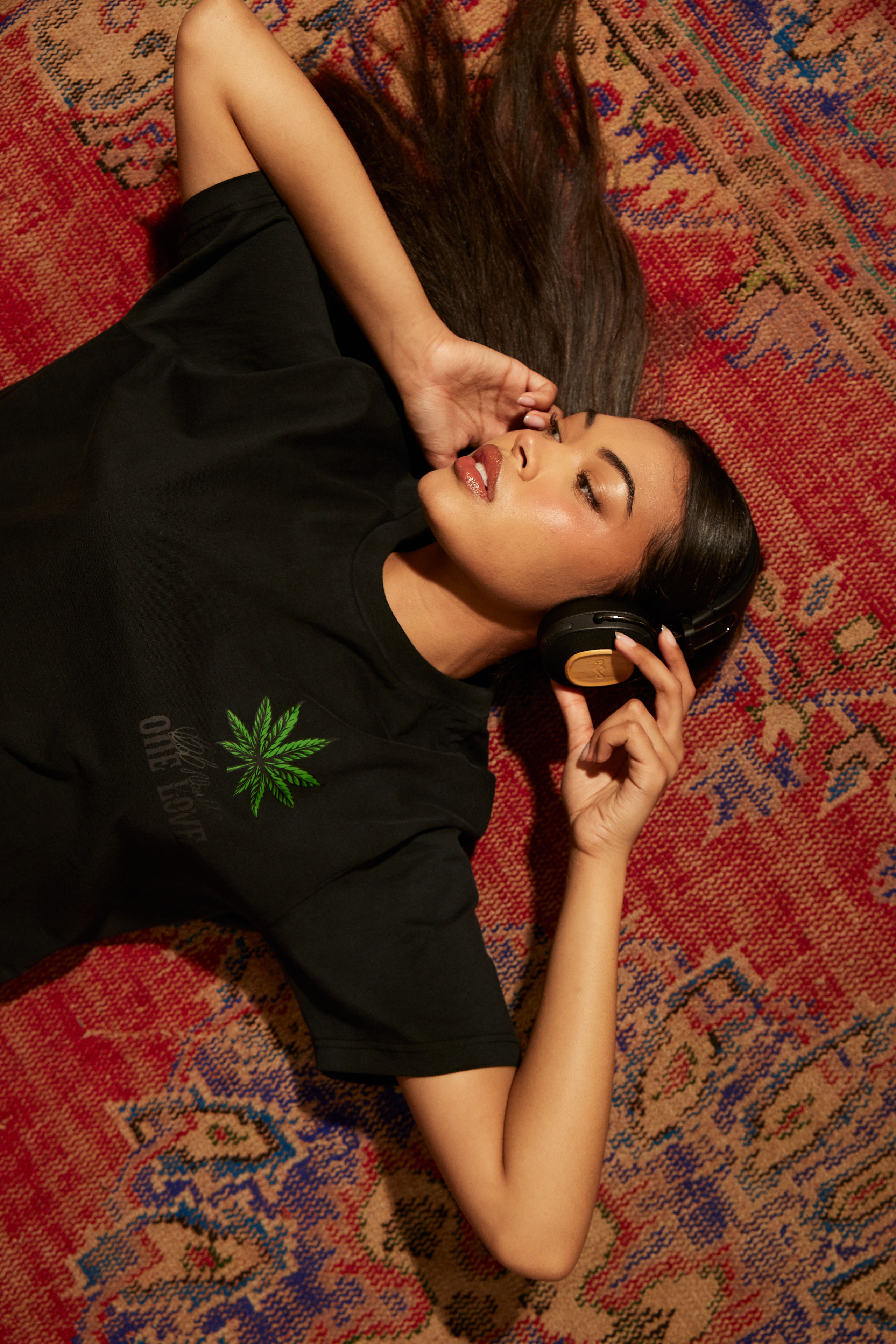 A woman lying on a rug, wearing a black shirt with a green leaf design.