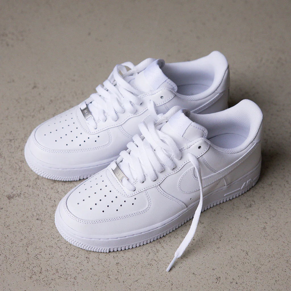 A pair of white Nike Air Force 1 sneakers on a concrete surface.