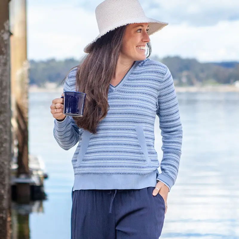 Woman in a striped sweater holding a mug by the water.