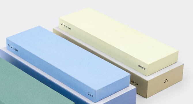 Close view of blue 1000-grit and cream Misen 6000-grit  Misen sharpening stones stacked on their storage boxes to show the stones’ width.