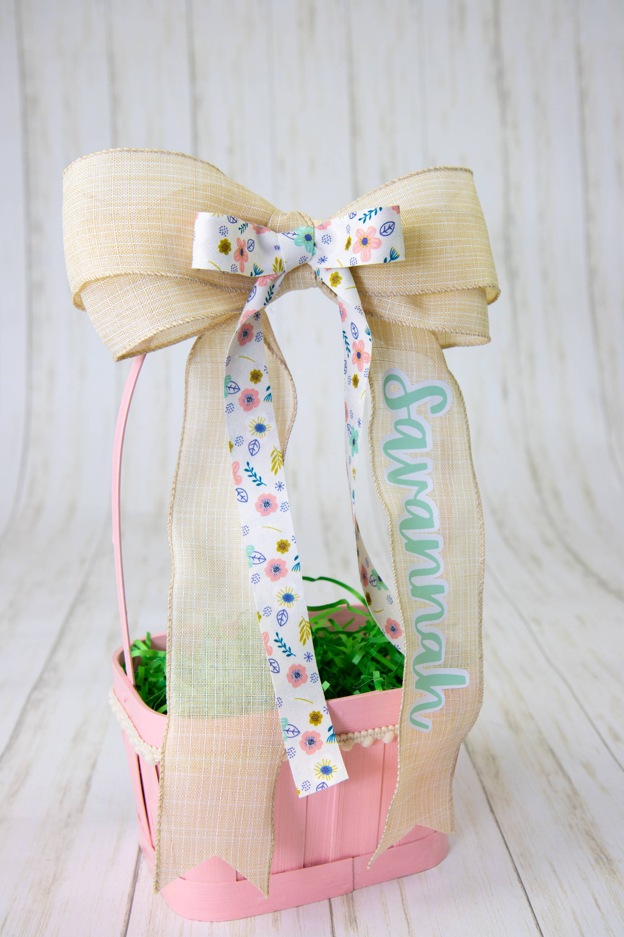 Pink Easter Basket that has a ribbon on it with the name Savannah in blue HTV and a smaller floral ribbon layered on top. 