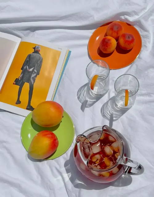 A picnic spread with fresh mangos and peaches and a jug of  fresh ice tea 
