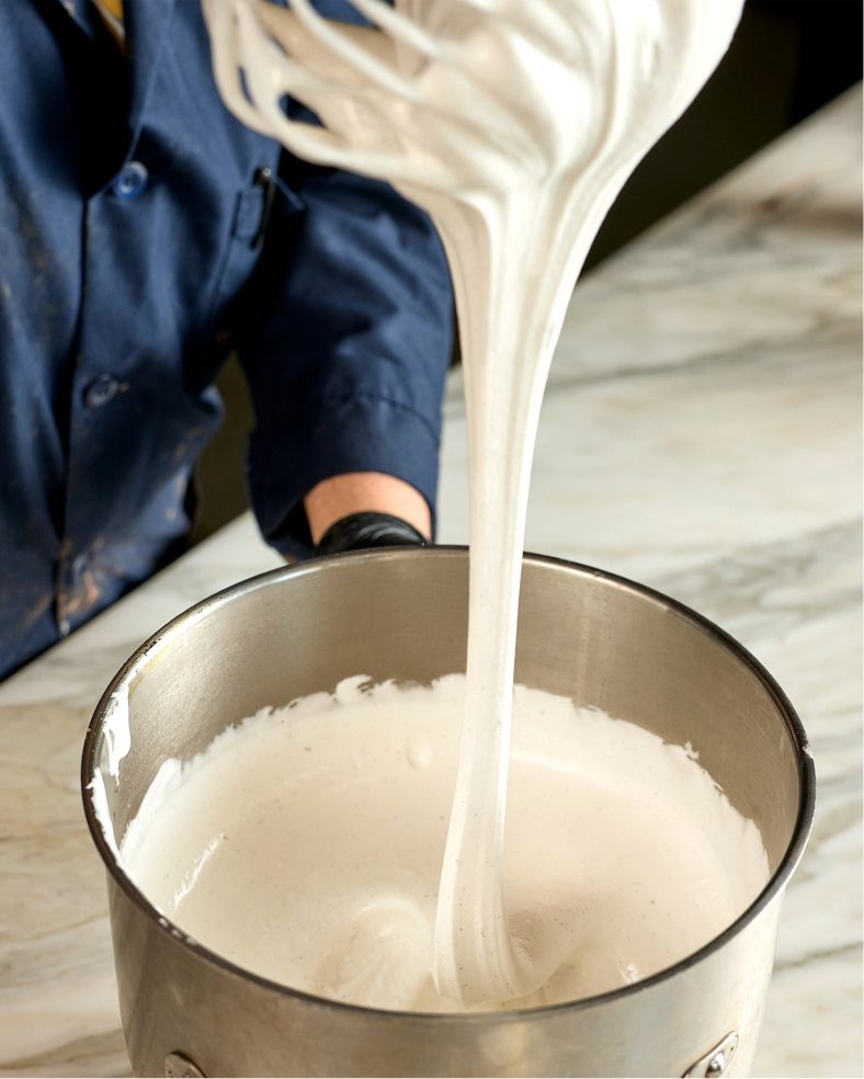 Person mixing a thick white substance in a metallic bowl.