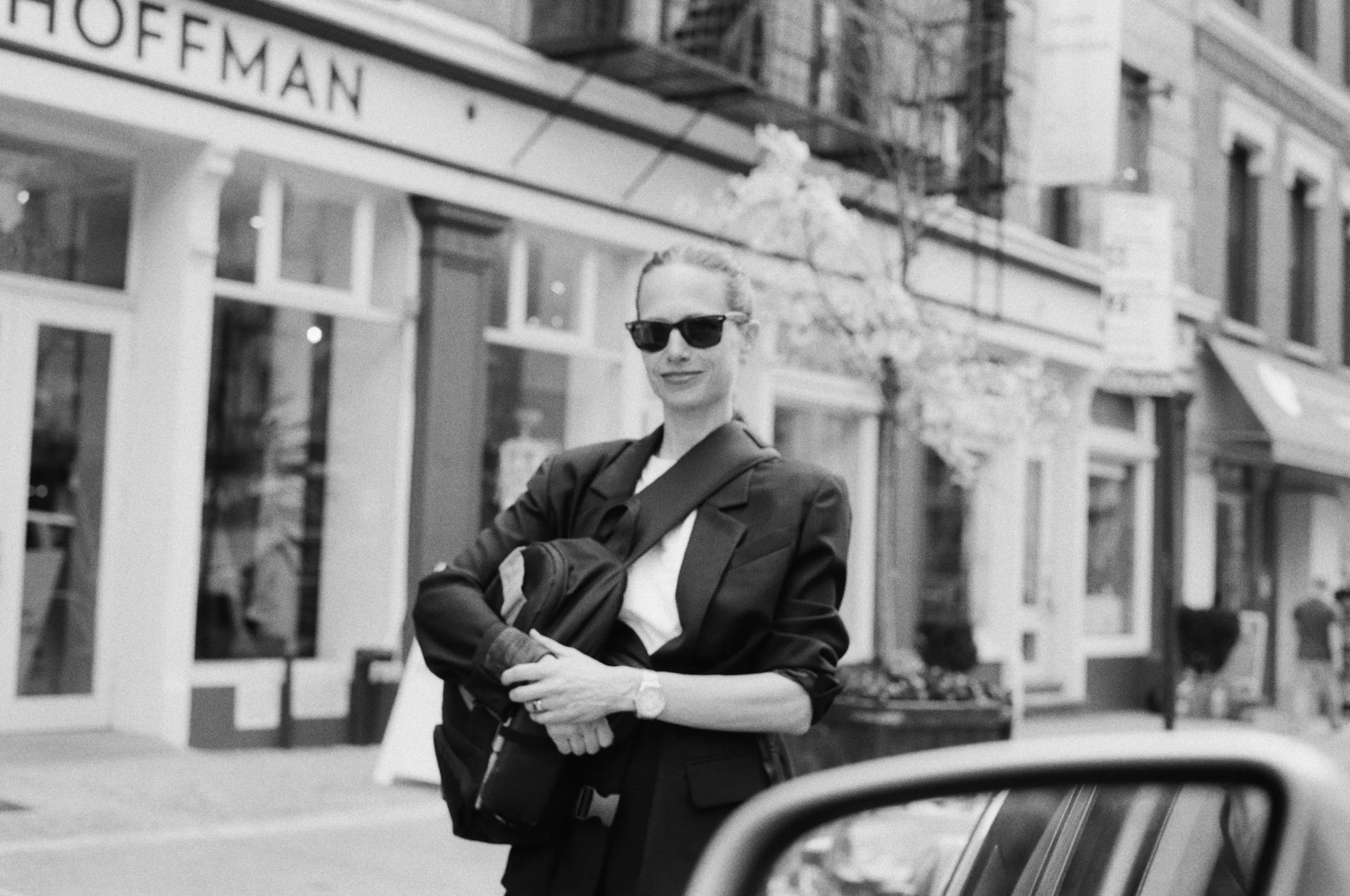 Person in sunglasses standing outside a store, holding a bag.