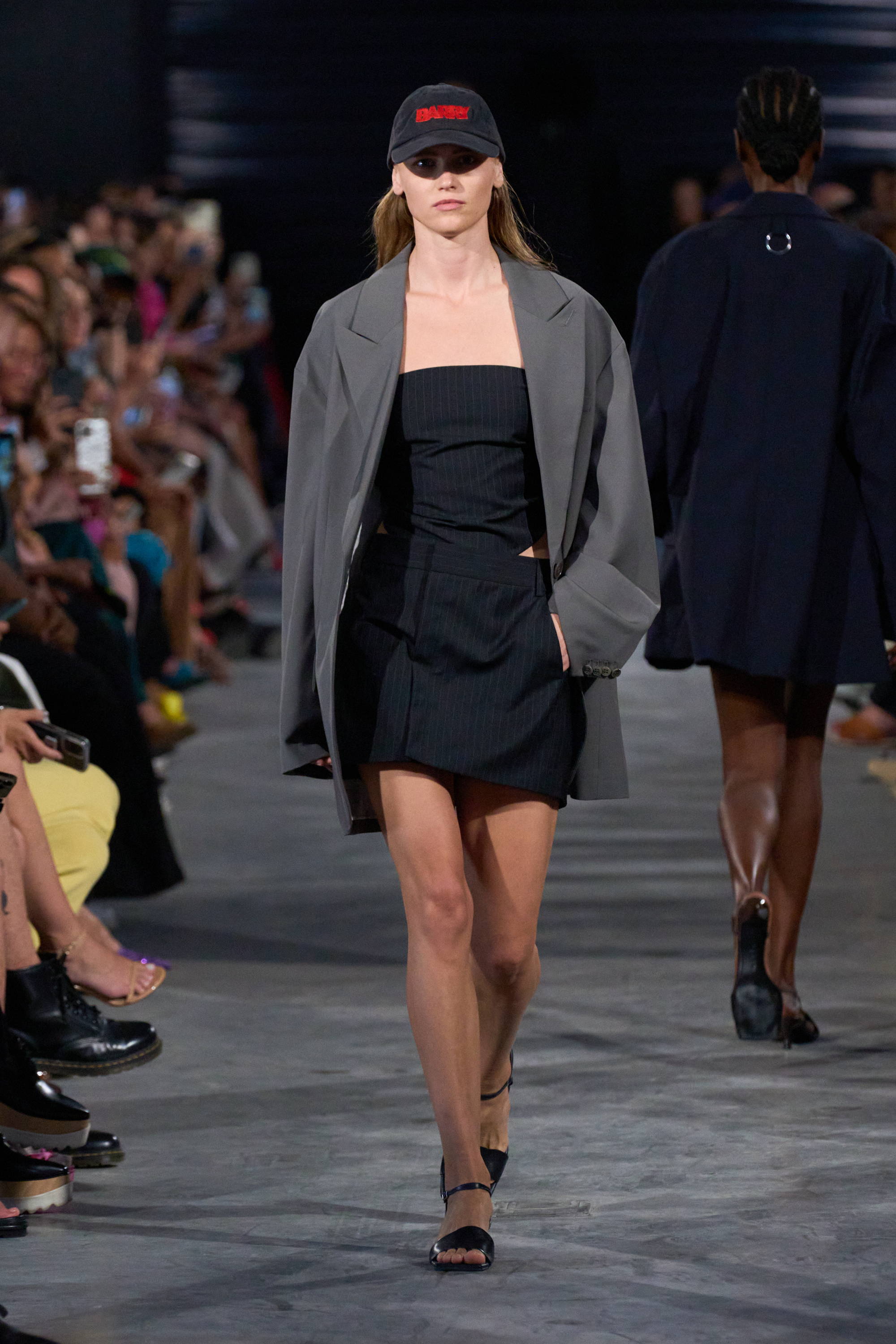 Model on a runway wearing cap, top, skirt, and blazer