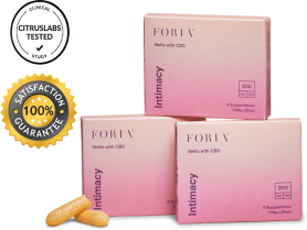 Three boxes of Foria Intimacy Melts with pink packaging design, one box stacked on top of the other two, two loose melts resting up against one of the boxes.
