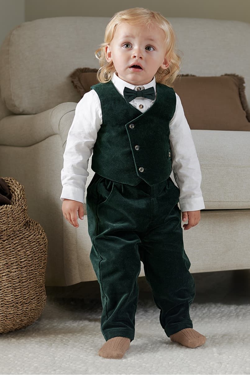 A young child in a green suit and bow tie, standing indoors.