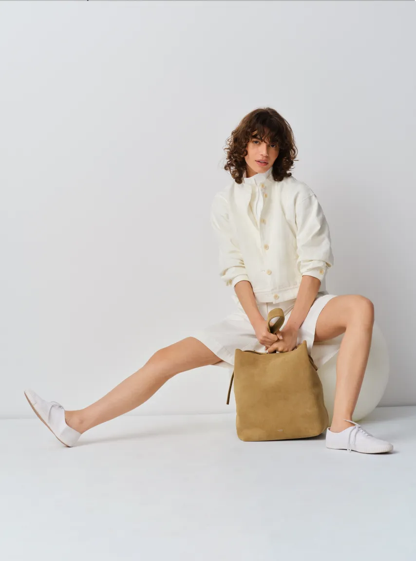 Model in casual outfit sitting with handbag on a white background.