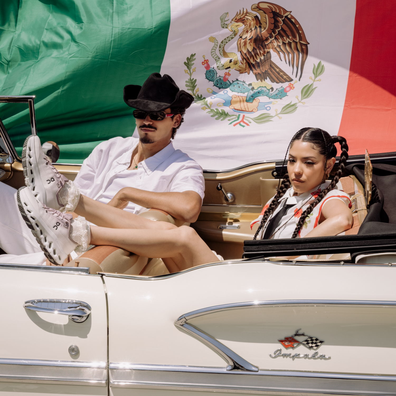 Couple in a classic car with a Mexican flag backdrop.