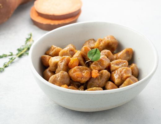 Bowl of gnocchi with herbs and sweet potatoes on a light surface.