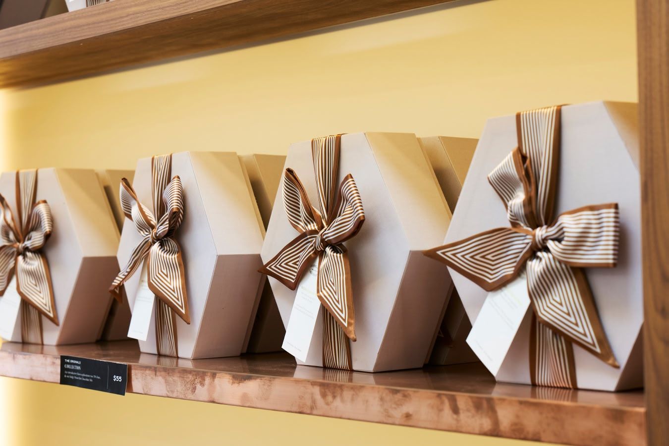 Four neatly wrapped gift boxes with ribbons on a wooden shelf.